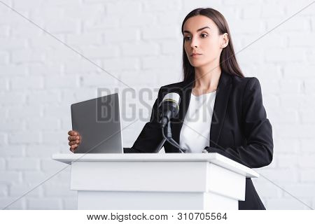 Attractive, Confident Lecturer Standing On Podium Tribune Near Microphone And Laptop