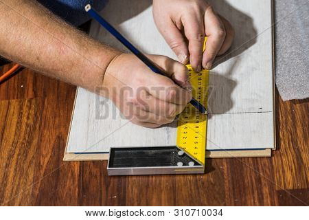 Construcion Worker Measuring Floor Panels Using Ruler And Pencil. Home Renovation Concept.