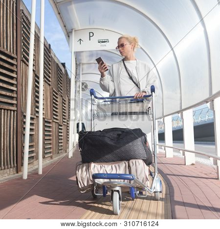 Young Casual Woman Using Mobile Phone Application While Transporting Luggage From Arrival Parking To