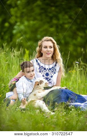 Mother Along With Her Little Son And Cub Of Newborn Lamb Posing Outdoors On Nature Background. Verti