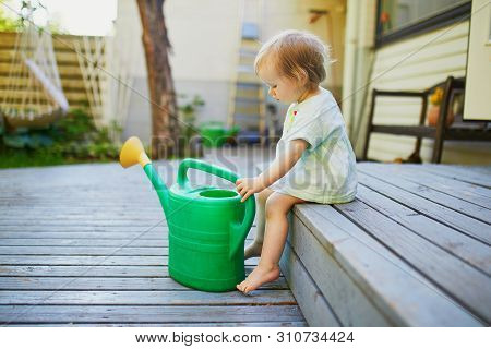 Cute Baby Girl Playing With Watering Pot A Warm Summer Day. Little Kid Helping Parents To Take Care 