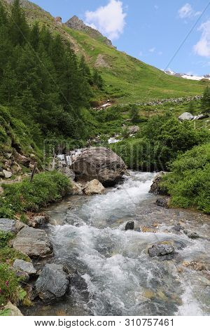 Predatory Mountain River In The Mountains Of The Taur Alps, Green Pasture With Blue Sky, Austria