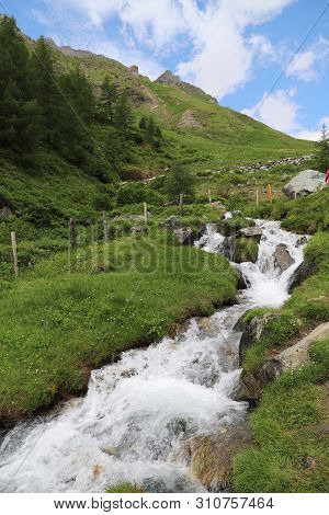 Predatory Mountain River In The Mountains Of The Taur Alps, Green Pasture With Blue Sky, Austria