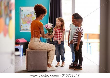 Group Of Elementary School Pupils Giving Female Teacher Thank You Gift Of Flowers