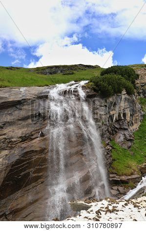 Predatory Mountain River In The Mountains Of The Taur Alps, Green Pasture With Blue Sky, Austria