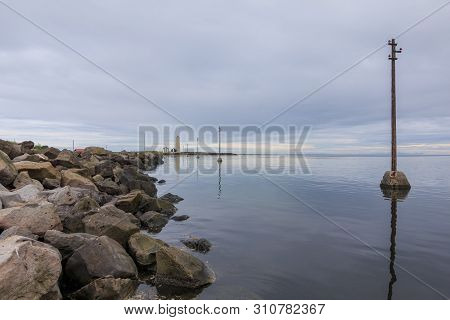 Island Grotta Near Reykjavik With Clouds In The Sky. Stony Coastline With Lighthouse And Houses To T