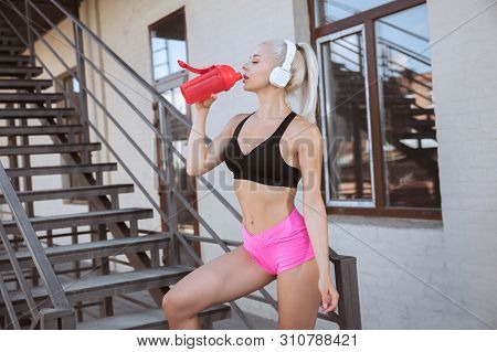 A Young Athletic Woman In White Headphones Working Out Listening To The Music On A Stairs Outdoors. 