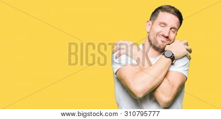 Handsome man wearing casual white t-shirt Hugging oneself happy and positive, smiling confident. Self love and self care