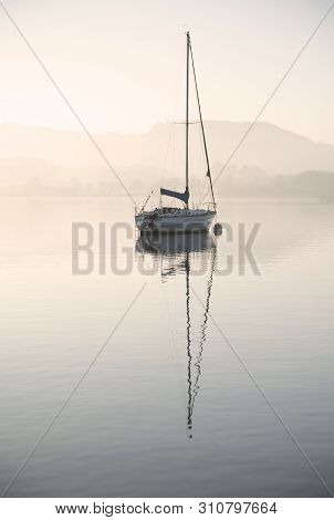 Beautiful Unplugged Landscape Image Of Sailing Yacht Sitting Still In Calm Lake Water In Lake Distri