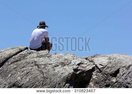 Man sitting on ock staring at the ocean in meditation