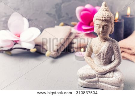 Decorative Buddha, Black Burning Candles, Towels  And Pink Magnolia Flowers On Grey Textured Backgro