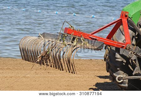 Tractor With Large Metal Rake Attached Sifting, Raking And Clearing Debris At A Public Beach In Earl