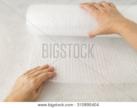 Woman Hands Unwind A Roll Of White Transparent Bubble Wrap On A Rough White Background. Material For