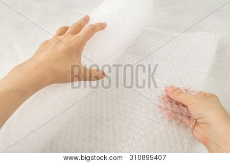 Woman Hands Hold A Roll Of White Transparent Bubble Wrap On A Rough White Background. Material For P