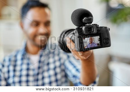 blogging, videoblog and people concept - smiling indian male video blogger with camera videoblogging at home