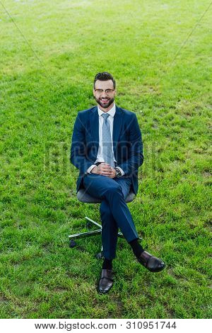 High Angle View Of Happy Young Businessman Sitting In Office Chair In Park And Loooking At Camera