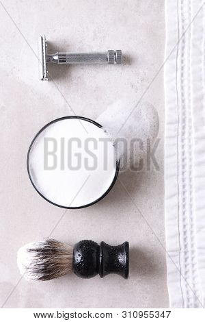 Shaving Still Life: Safety razor with towel, brush and soap on a gray tile surface.