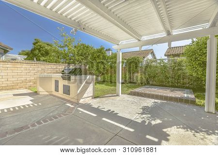 Concrete Patio Of A Home With Barbecue Grill And White Wooden Pergola
