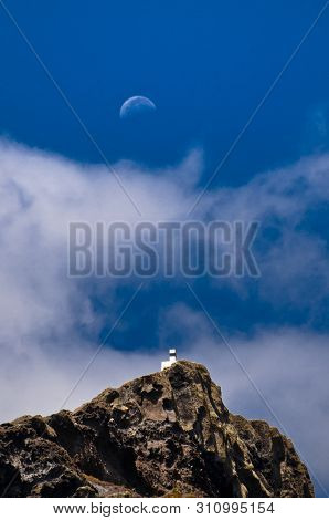 The Moon Is Rising Up Above A Small White House On The Hill