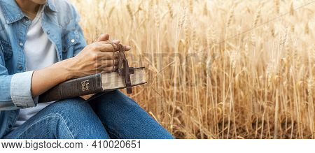 Christian Woman Praying On Holy Bible And Wooden Cross In Barley Field On Summer. Woman Pray For God