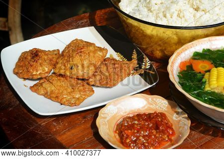 Fried Tempe With Homemade Sambal Terasi, Rice, And Spinach Corn On A Wooden Table