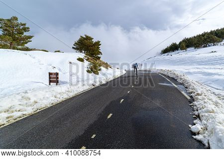 Cyclist Climbing Snowy High Mountain Pass. La Morcuera, Madrid.