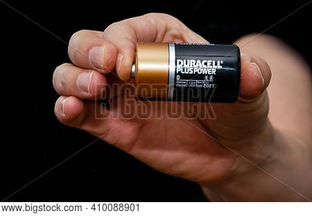 Close Up Of A Hand Holding A Duracell Battery, Isolated On A Black Background.