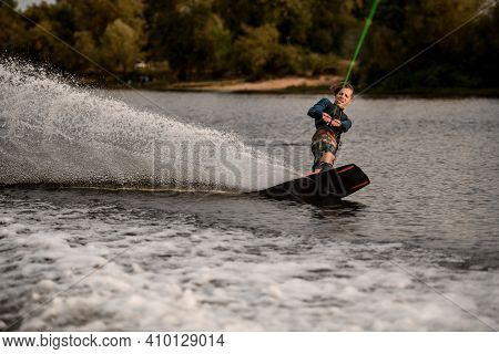 Sportive Guy Holding Taut Rope And Rides Down On Wave On Wakeboard