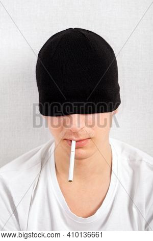 Young Man In A Hat With A Cigarette By The White Wall Closeup