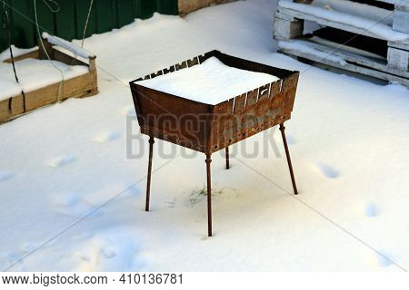 Rusty Barbecue In The Yard In Winter. The Brazier Is On The Street. Metal Mangla On Four Legs, Rusty