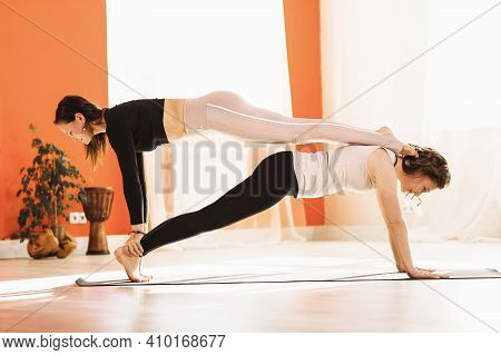 Two Women Yoga Practitioners Perform The Kumbhakasana Pair Exercise With One Person On Top Of The Ot