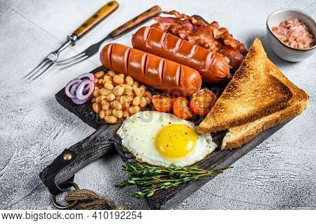 Full Fry Up English Breakfastt With Fried Eggs, Sausages, Bacon, Beans And Toasts On A Wooden Cuttin