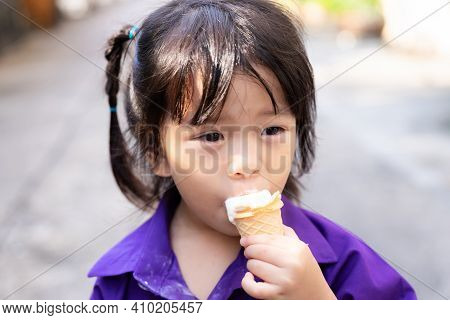 Candid Adorable Girl Eat Ice Cream Cone In The Heat After School. In Summertime. A 3-4 Years Old Kid