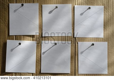 Six Note Paper Stickers Are Screwed To The Brown Cardboard With Metal Screws. White Blank Square She