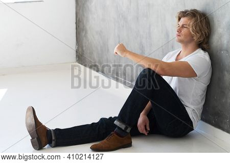 Young handsome man model wearing jeans and white thirt sitting on the floor. Studio fashion portrait. Lifestyle and people concept.