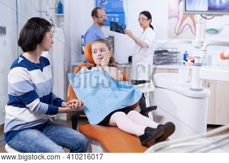 Little Kid With Painfull Expression Touching Face During Professional Dental Treatment. Child With H
