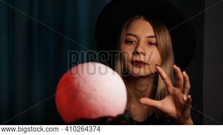 A Young Woman Fortune Teller In A Hat Is Holding A Magic Ball. Beautiful Psychic Woman Is Guessing W