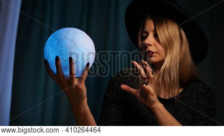 A Young Woman Fortune Teller In A Hat Is Holding A Magic Ball. Beautiful Psychic Woman Is Guessing W