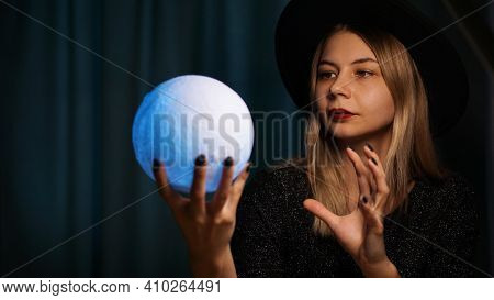 A Young Woman Fortune Teller In A Hat Is Holding A Magic Ball. Beautiful Psychic Woman Is Guessing W
