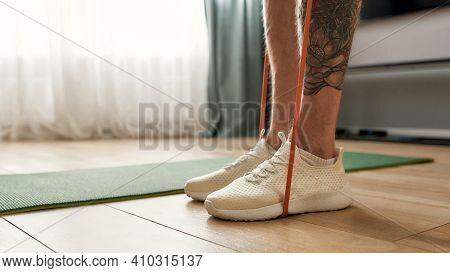 Athletic Man Standing On An Elastic Band And Working Out At Home. Man Doing A Workout At Home While 