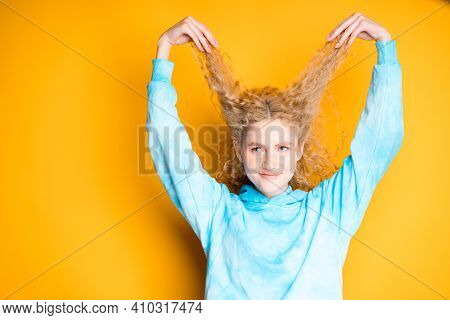 Beautiful Woman In A Blue Sweater Pulls Her Curly Hair Up By Raising Her Hands Up