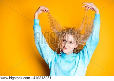 Beautiful Woman In A Blue Sweater Pulls Her Curly Hair Up By Raising Her Hands Up