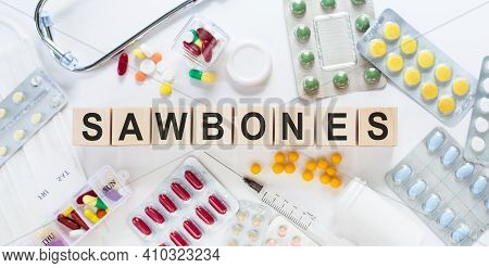 Sawbones Word On Wooden Blocks On A Desk. Medical Concept With Pills, Vitamins, Stethoscope And Syri