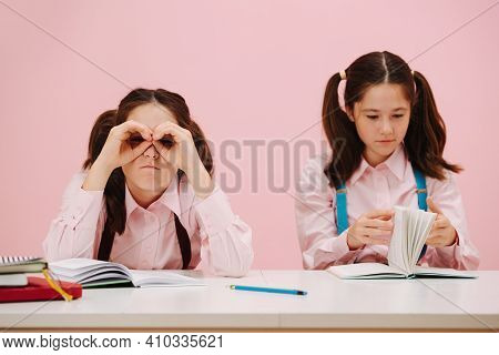 Bored Twin Schoolgirls Sitting Behind Schooldesk. One Making Hand Binoculars