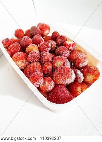 Close Up Of Frozen Strawberries With Frost On Them In A Plastic Container On White Background