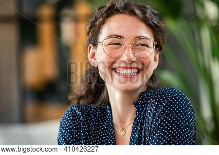 Portrait of laughing young woman wearing spectacles in office. Carefree casual girl wearing glasses and looking away. Confident beautiful student wearing specs and smiling.