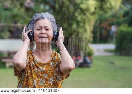 Senior Woman With Short Gray Hair Wearing Wireless Headphones Listening To A Favorite Song, Smiling 