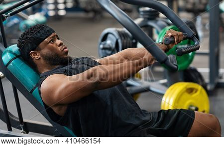 Athletic Young Black Man Having Workout On Chest Press Machine In Gym, Pushing Weight While Reclinin