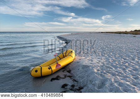 Yellow packraft rubber boat with red padle on a sea coast. Packrafting. Active lifestile concept