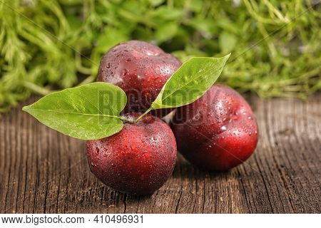 Three red plums with green leafs on wooden board